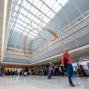 Curved metal sculpture suspended from the ceiling above passengers on a concourse